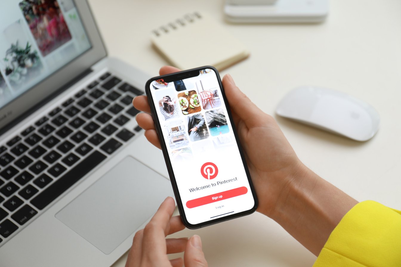 MYKOLAIV, UKRAINE - AUGUST 28, 2020: Woman Holding IPhone 11 with Pinterest App on Screen at Table, Closeup